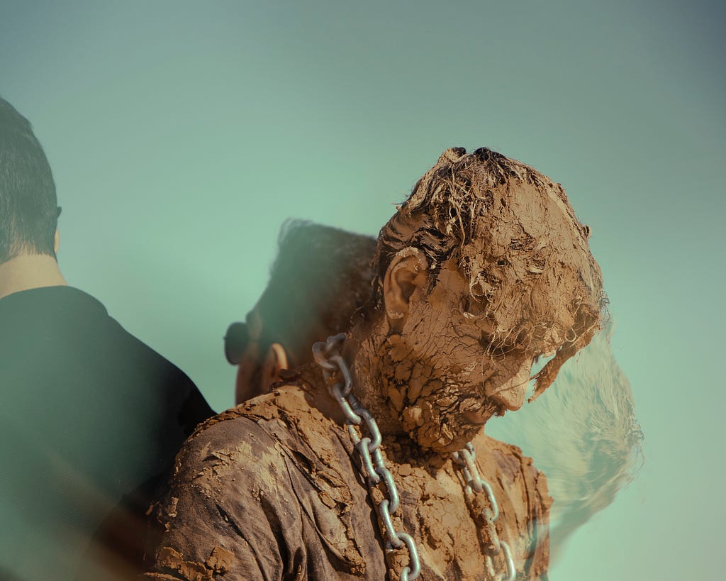 Mud-caked man with chain around his neck.