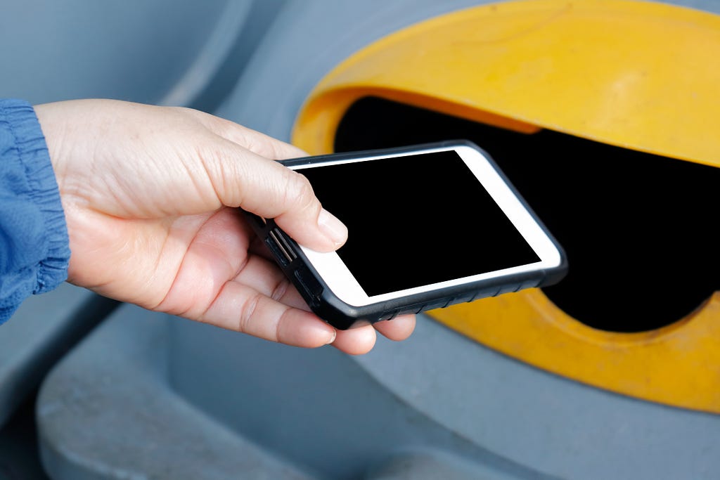 A hand begins to place a smartphone in a specialised recycling bin.