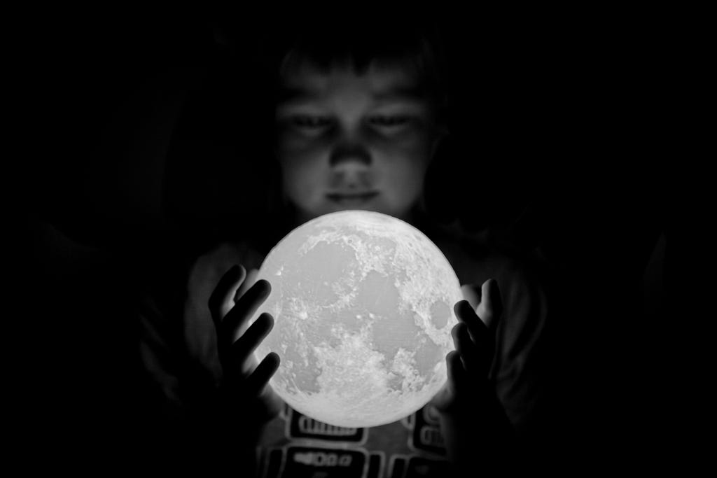 Black and white photo of a young boy holding a moon figure in his hands.