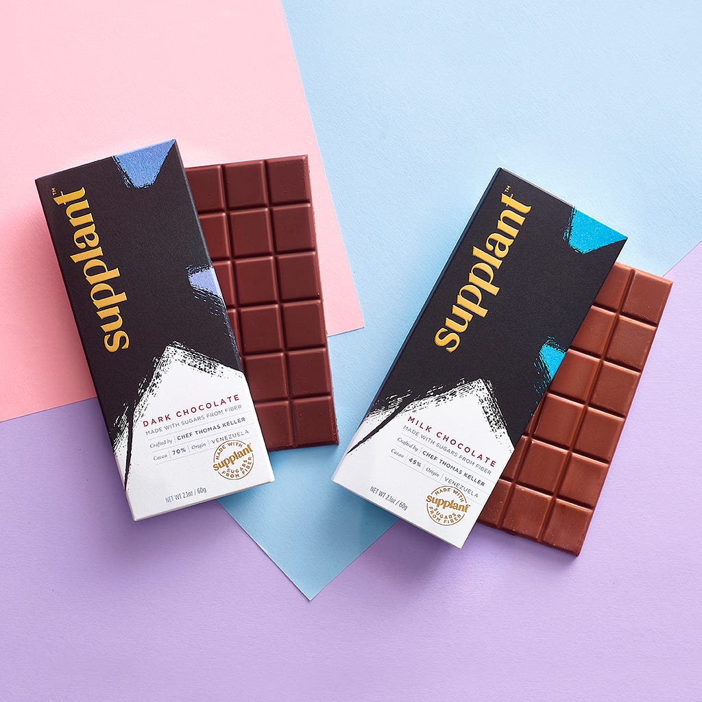 A dark chocolate bar and a milk chocolate bar on a pink and blue background.