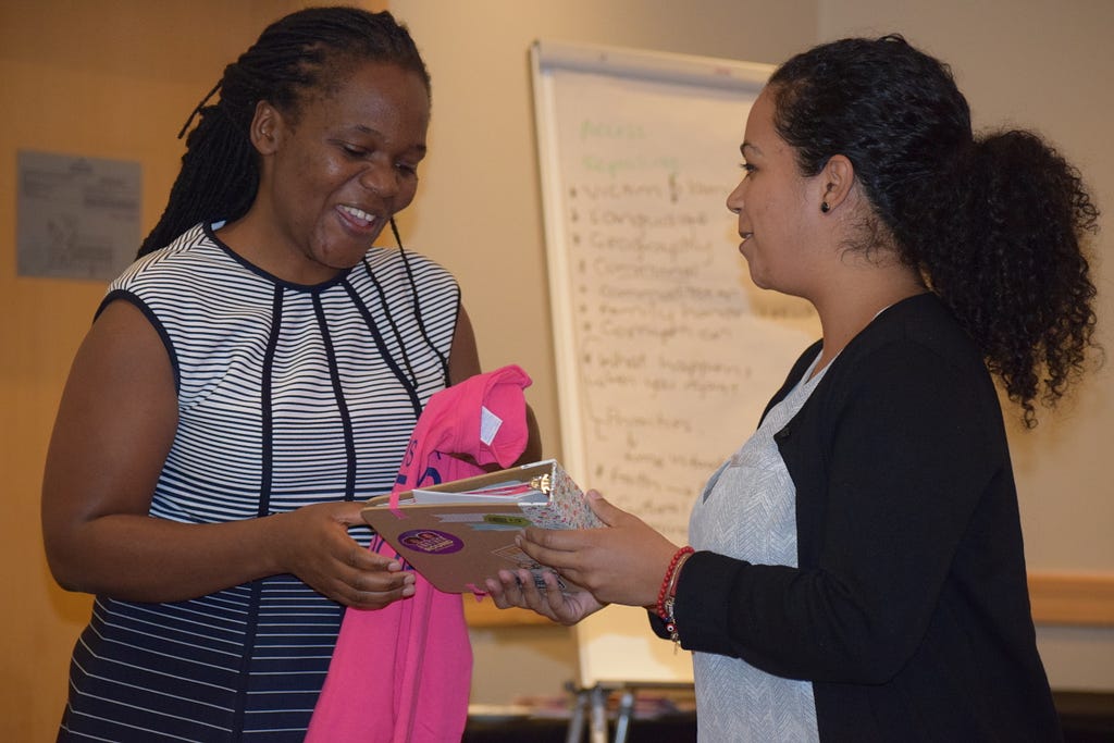 Photograph of Lorena Estrella handing Talent Jumo a pink t-shirt and a notebook of well wishes from young people in New Jersey