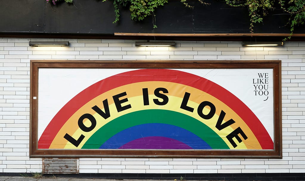 Big poster or Small billboard of Love is love written inside a rainbow in what could be a train station