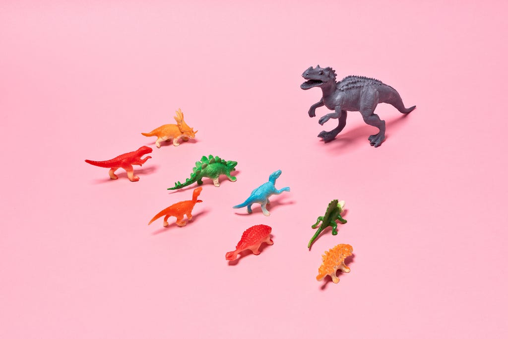 A photo of smaller dinosaur figurines in front of a T-rex figurine.