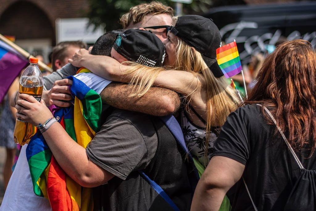 people, holding pride flags, hugging each other in the middle of a crowd
