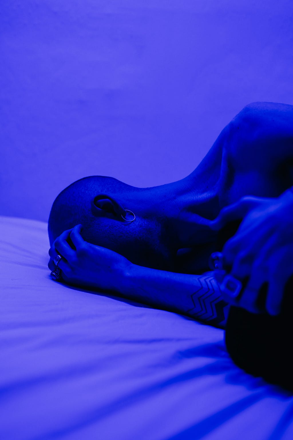 Uma foto de uma pessoa em uma cama com a mão sobre o rosto e iluminada por uma luz rox