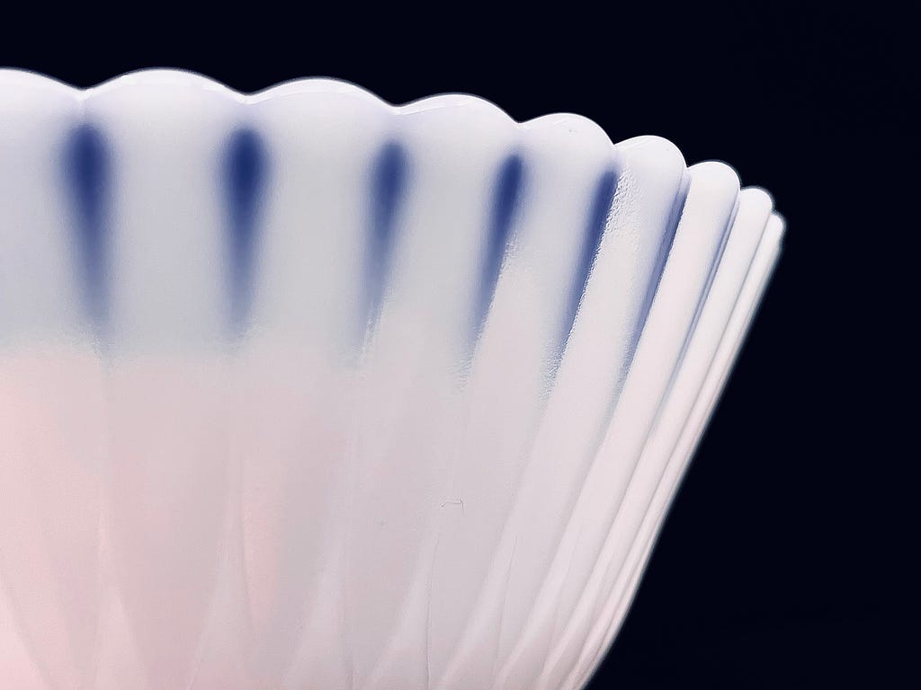 A close up view of the translucent, scalloped edge of a Petalware compote dish in Monax white against a black backdrop.