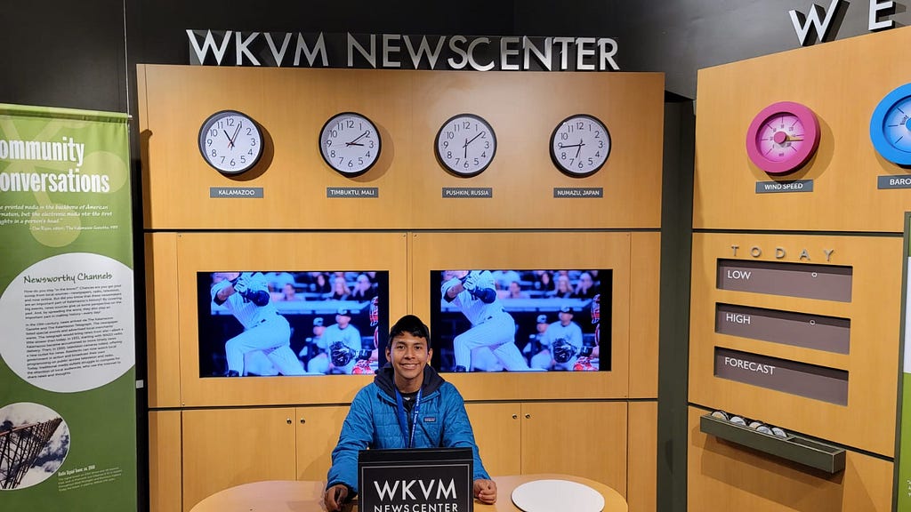 A young adult poses in front of a news center display at a museum.