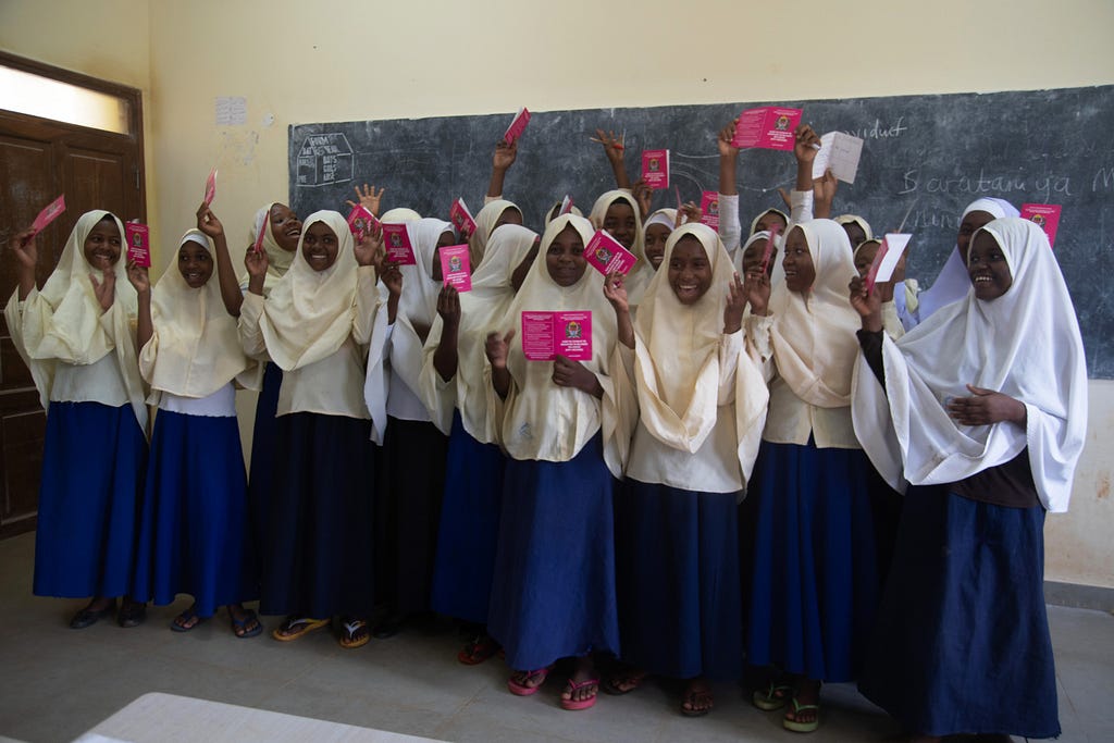 A group of girl students at Donge School, in Zanzibar, holding up pink pamphlets and smiling after receiving their HPV vaccines.