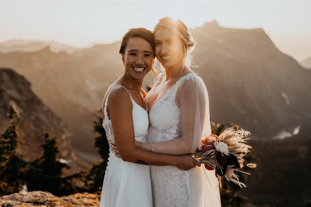 Quyen and her wife Amy posing for a photo in white wedding gowns after their elopement in the Northern Cascades