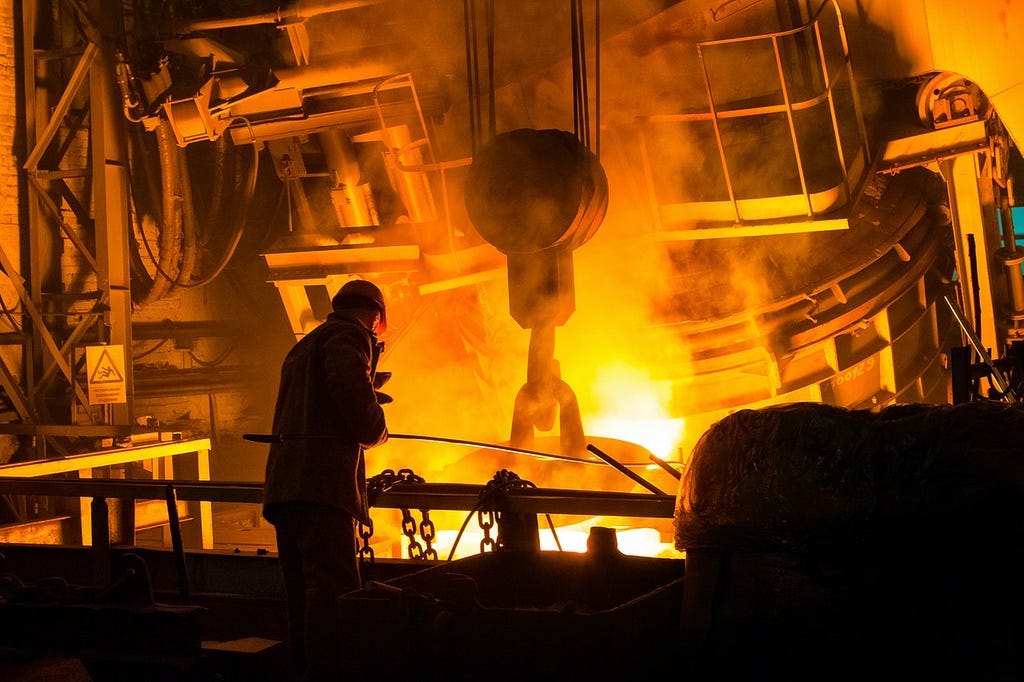 Silhoueatte of a worker in front of a glowing steel furnace