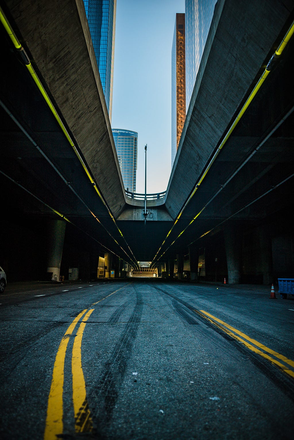 Picture taken from under an overpass in Downtown L.A. that shows the street below with some skid marks and the freeway lanes above on either side of the frame.