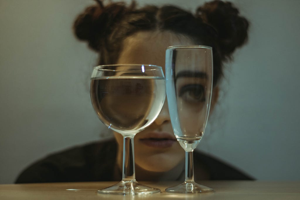 a person crouches behind two glasses of clear water