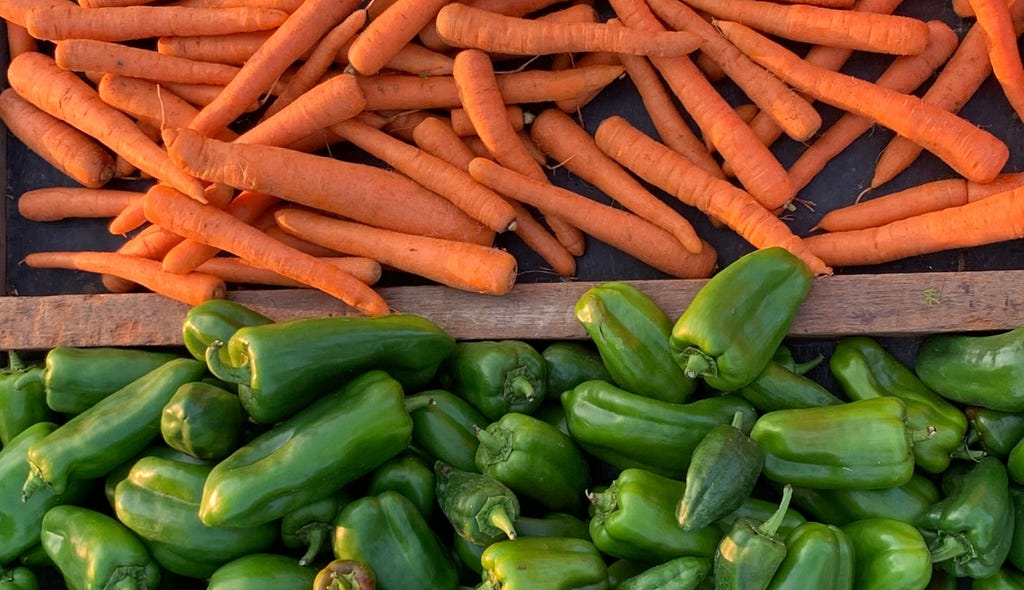 Tabuleiro de feira com cenouras e pimentões verdes.