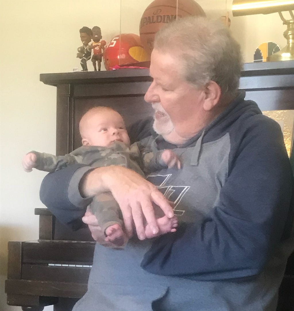 Jeff holds his grandson, Jones, while sitting on the piano bench.