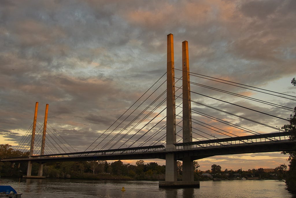 A cable-stayed bridge during a cloudy sunset with the tips of the bridge illuminated with a bit of golden hour sunshine