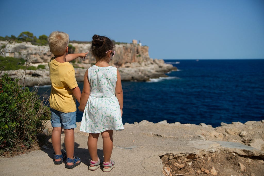 two children holding hands looking out into the ocean