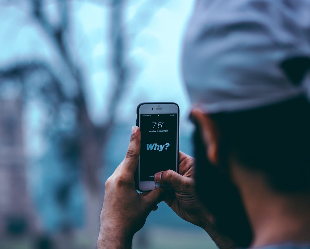 A person holding a mobile phone reading the the word why by Abhay Gautam