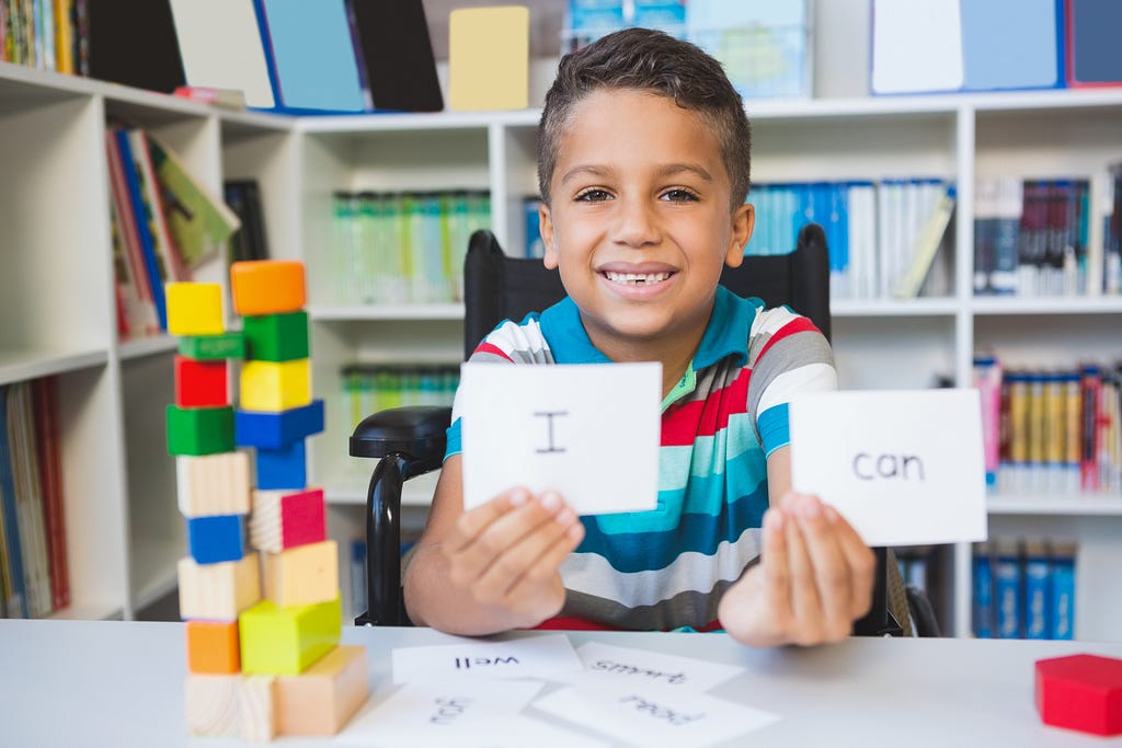 Boy in wheelchair showing cards that reads “I Can”