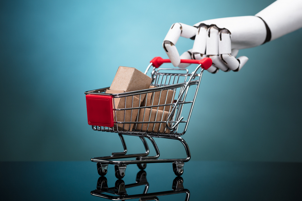 A large robotic hand pinches a tiny shopping cart filled with parcels.