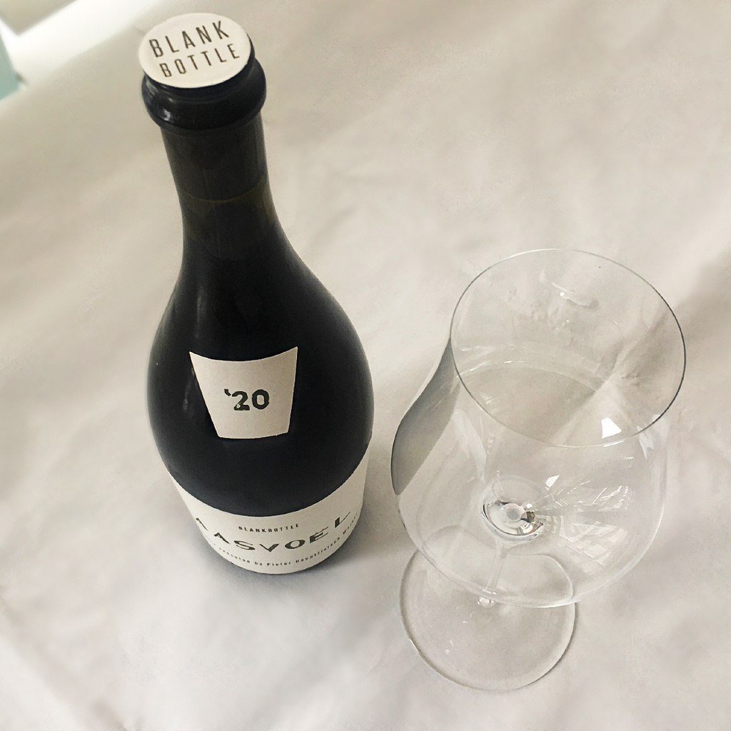 Closed bottle of Aasvoël 2020 next to an empty wine glass