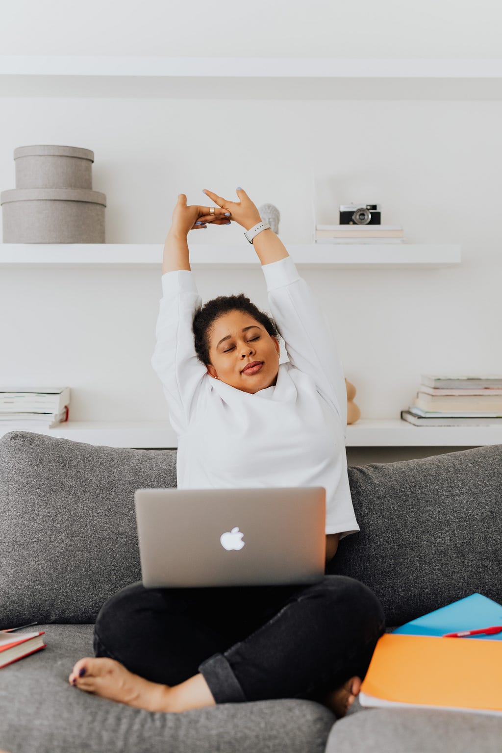 Woman stretching her arms on a couch with a laptop in her lap