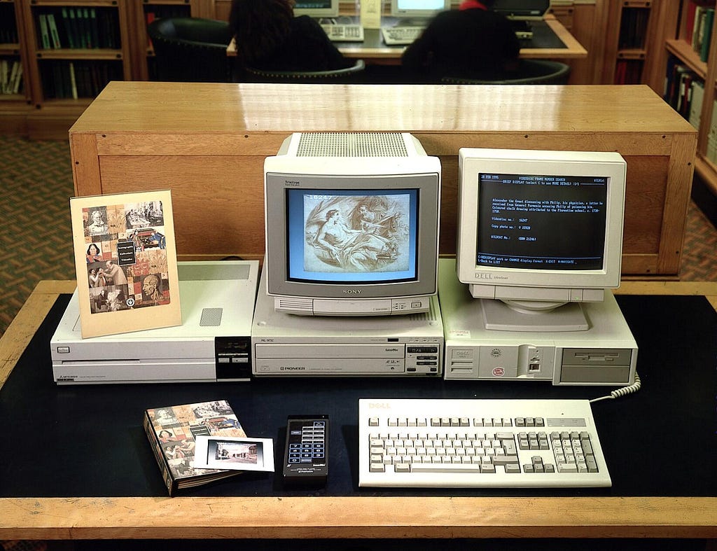 Three old computers on a wooden desk in the library. There are two monitors, one showing a digital image — some sort of engraving — the other showing some text. Next to them is the “Iconographic Library Videodisc”, which was an output of our early digitisation programme.