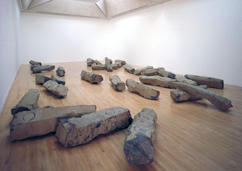 A large installation consisting of thirty-one rough, bulky basalt rocks, which are strewn across the floor in a seemingly ran