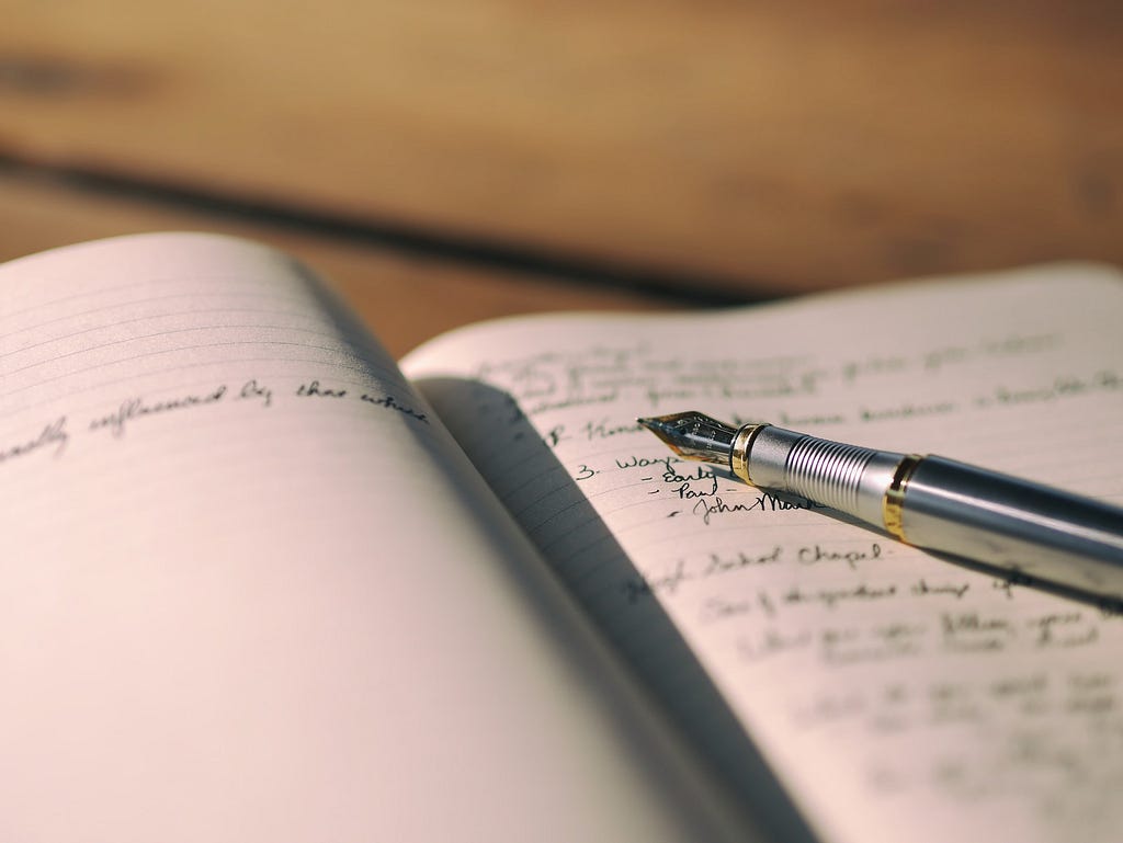 Open journal with a silver fountain pen on top of it. There is some writing on both pages in cursive.