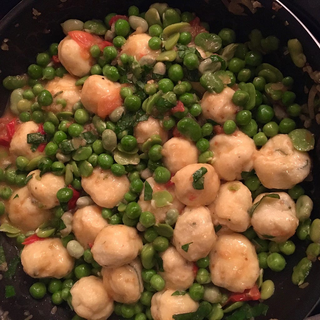 Overhead view of a pan filled with bite-sized dumplings and peas.