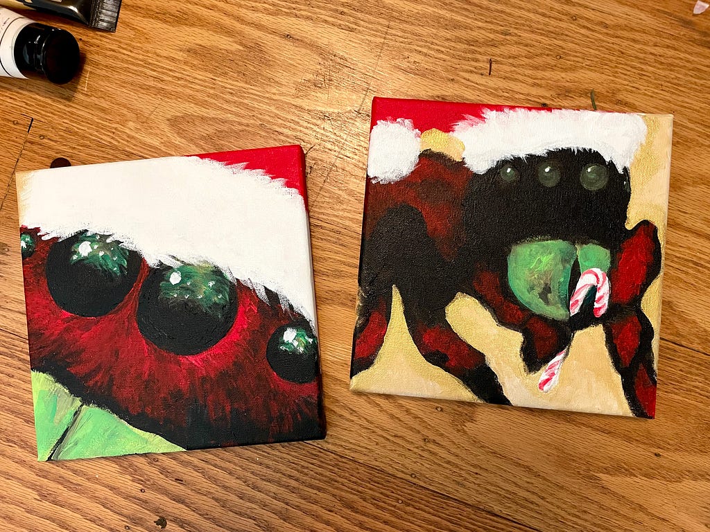 Two small canvases show different versions of a christmas spider. Both spiders wear santa hats. One is shown in an extreme close up, with a christmas tree reflecting in its eyes. It has a dark red furry face and green mandibles. The other spider is shown in three quarters view. It is black and red striped, with green mandibles. It is holding a candy cane.
