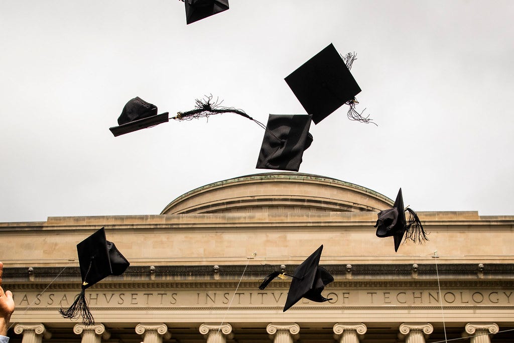 Photo of the MIT Great Dome with graduation caps flying in the air in front.