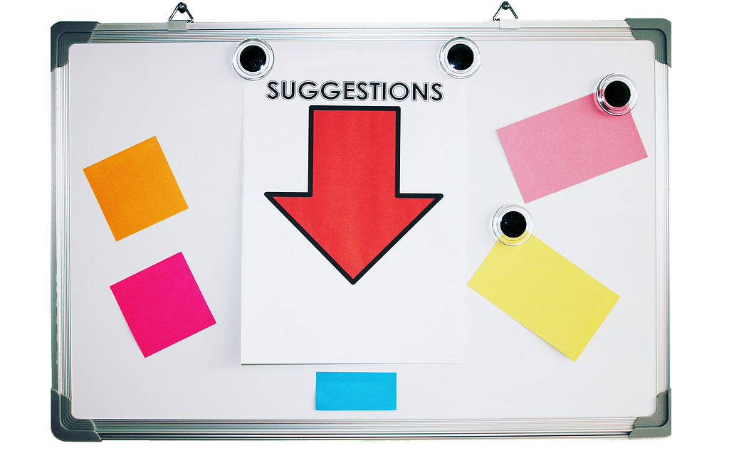 A whiteboard with orange, yellow, pink, and blue sticky notes on it and a paper with a red arrow that reads suggestions.