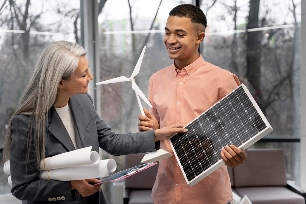 Two business professionals discussing renewable energy solutions. The man, holding a solar panel, smiles as he explains something to the woman, who is holding a small model wind turbine and several rolled-up documents. They are standing in a modern office with large windows, providing a view of trees outside. The image highlights collaboration and innovation in the field of sustainable energy.