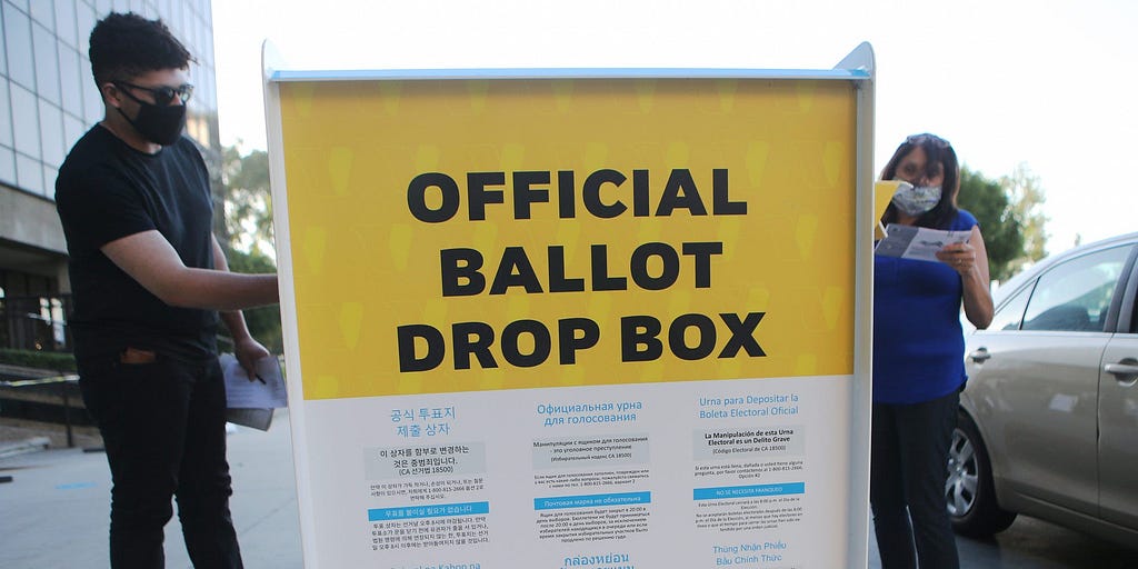 Pedestrians place ballots in a  mail-in ballot drop box outside of the L.A. County Registrar’s office.