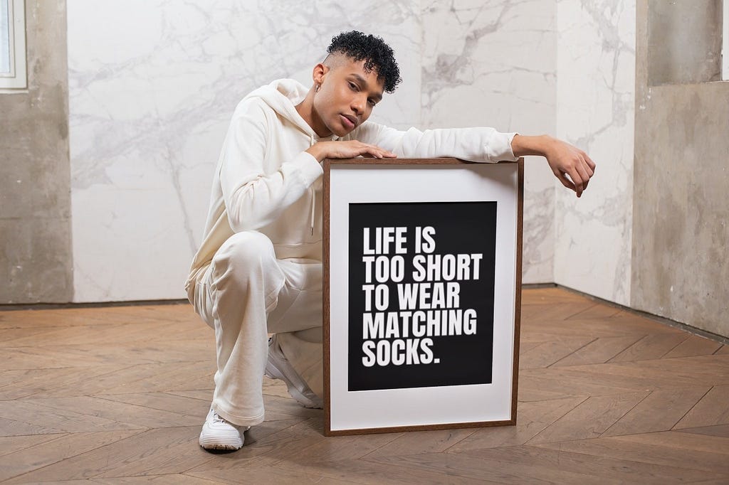 A man holding a wall art of the phrase “Life is too short to wear matching socks”.