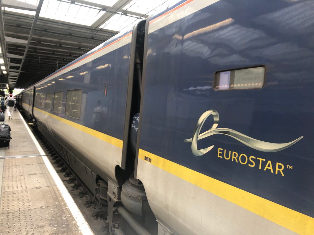 Eurostar train waiting at a platform. A few passengers are walking by wheeling suitcases.