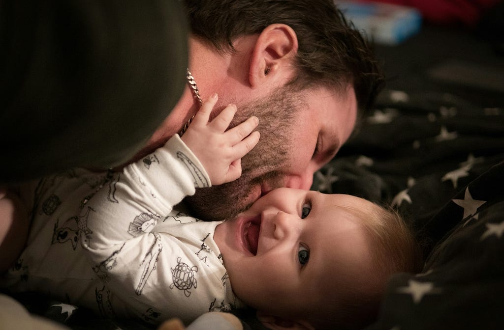 A man kissing a laughing baby on the cheek