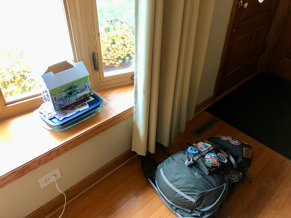 Author’s photo of a few items piled near the front door: hiking backpack, baking dish, Halloween decoration packaging.