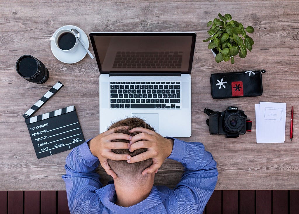 A frustrated writer sitting in front of a notebook, holding his head in hands.