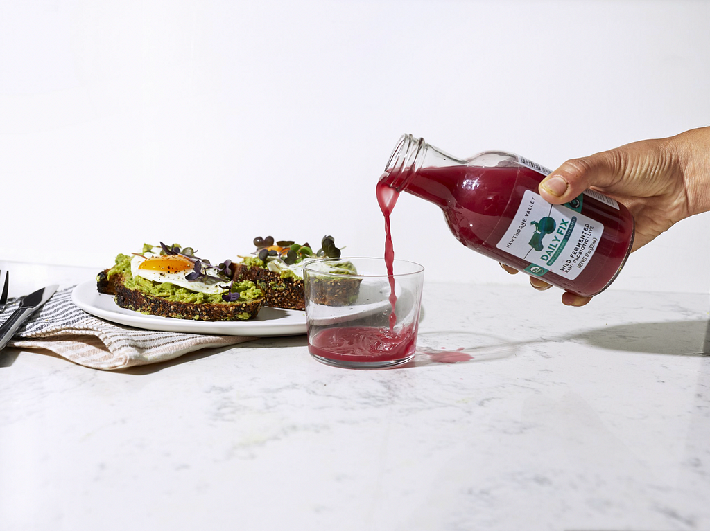 Disembodied hand pours beet red fermented drink into glass on white marble countertop