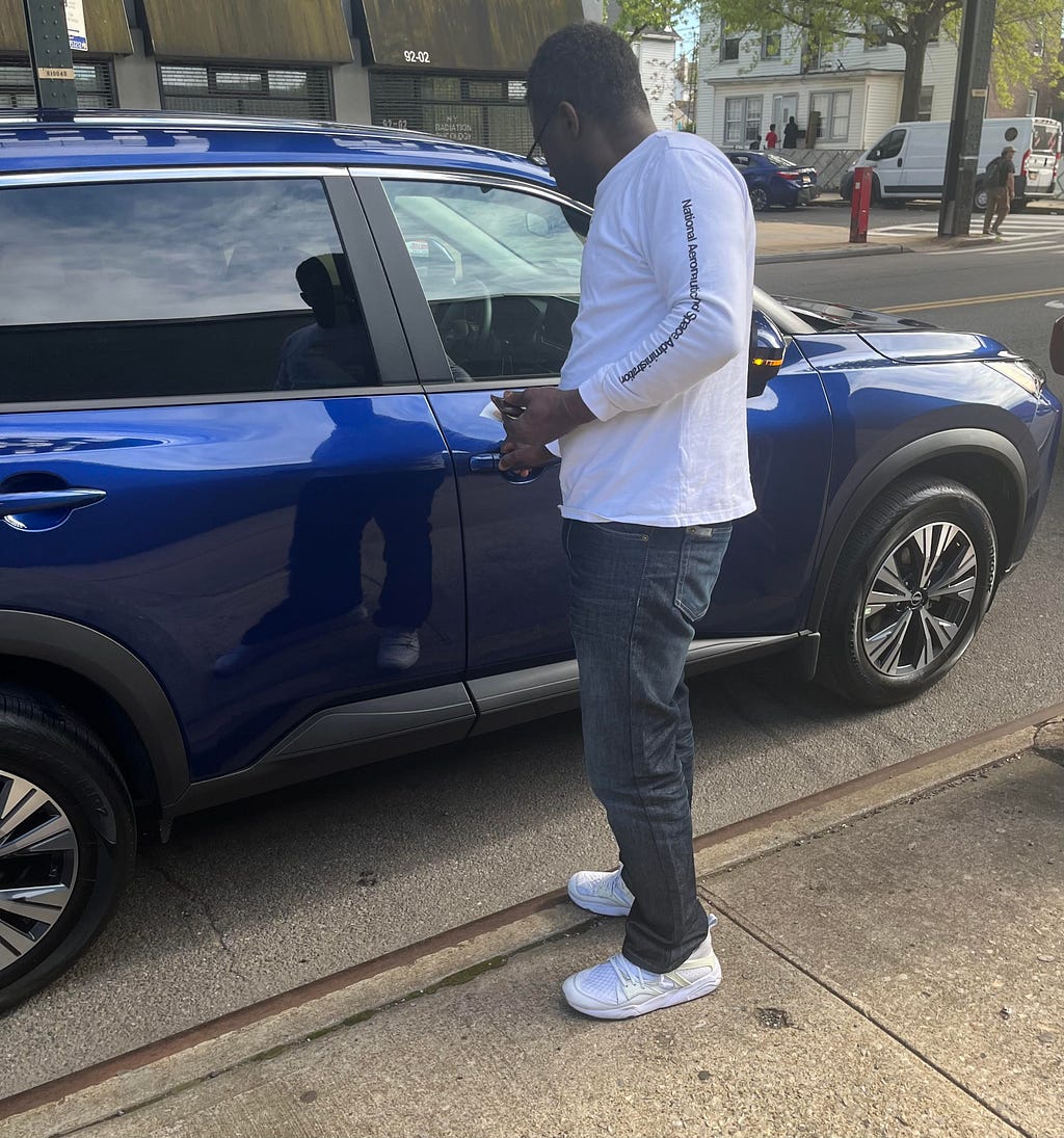 Dark skinned man putting key into car lock on passenger side of navy blue SUV cross vehicle.