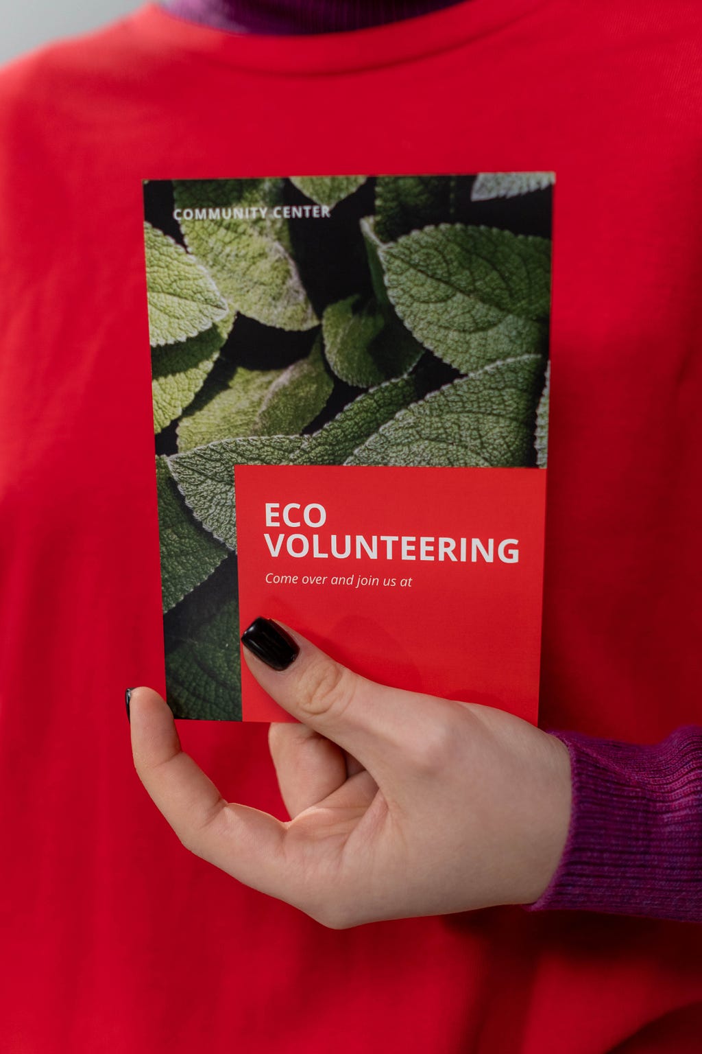 a hand holding a card that reads “ECO VOLUNTEERING come over and join us”