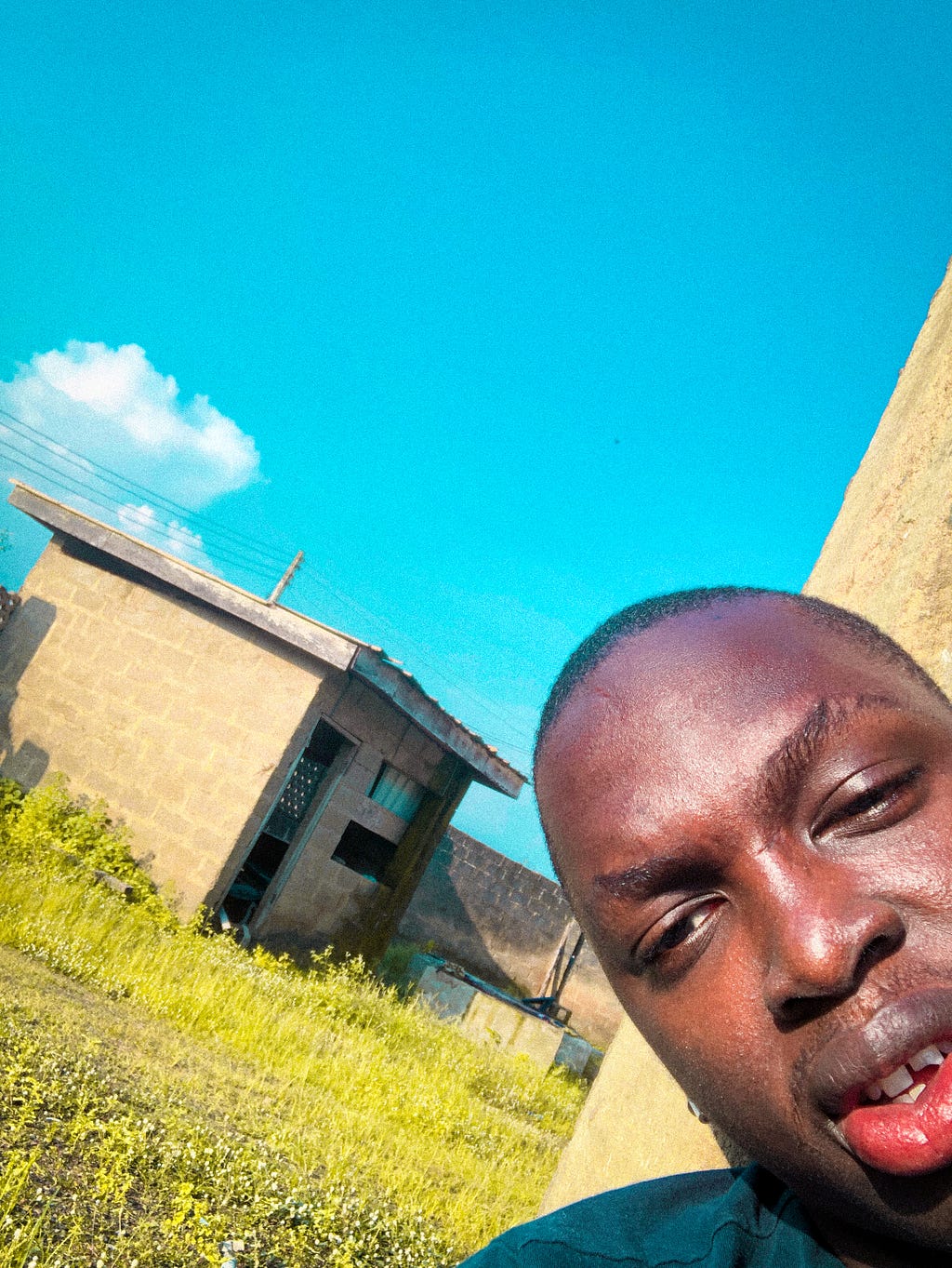 A picture of me sitting at home, the background is made up of the blue sky, green grass and a construction shed. Circa 2020. It reminds me of Mr Eazi’s “One day you will understand” cover art.