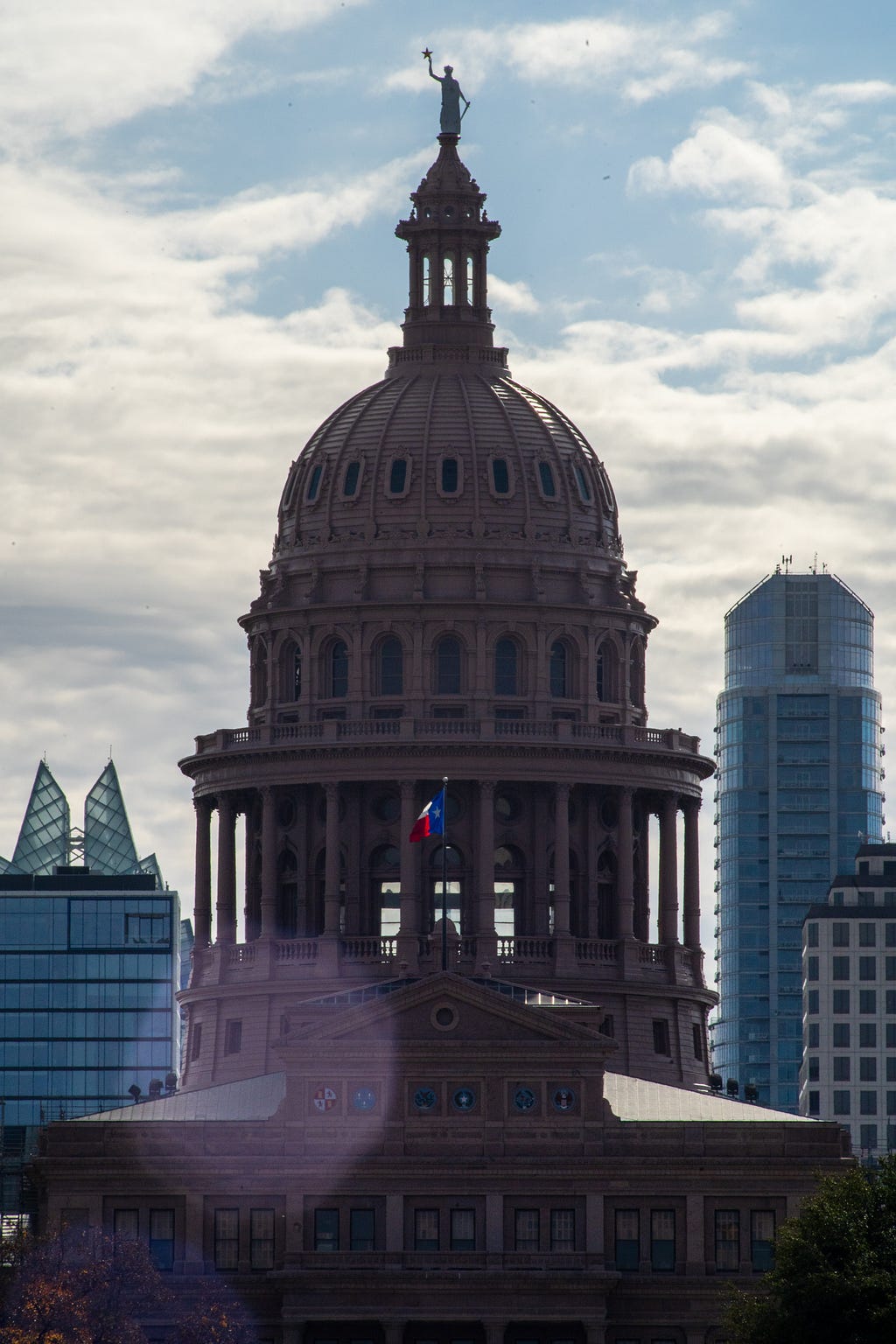 A telephoto picture of the top of the Texas State Capitol in Austin, Texas. The skyline looming in the background.