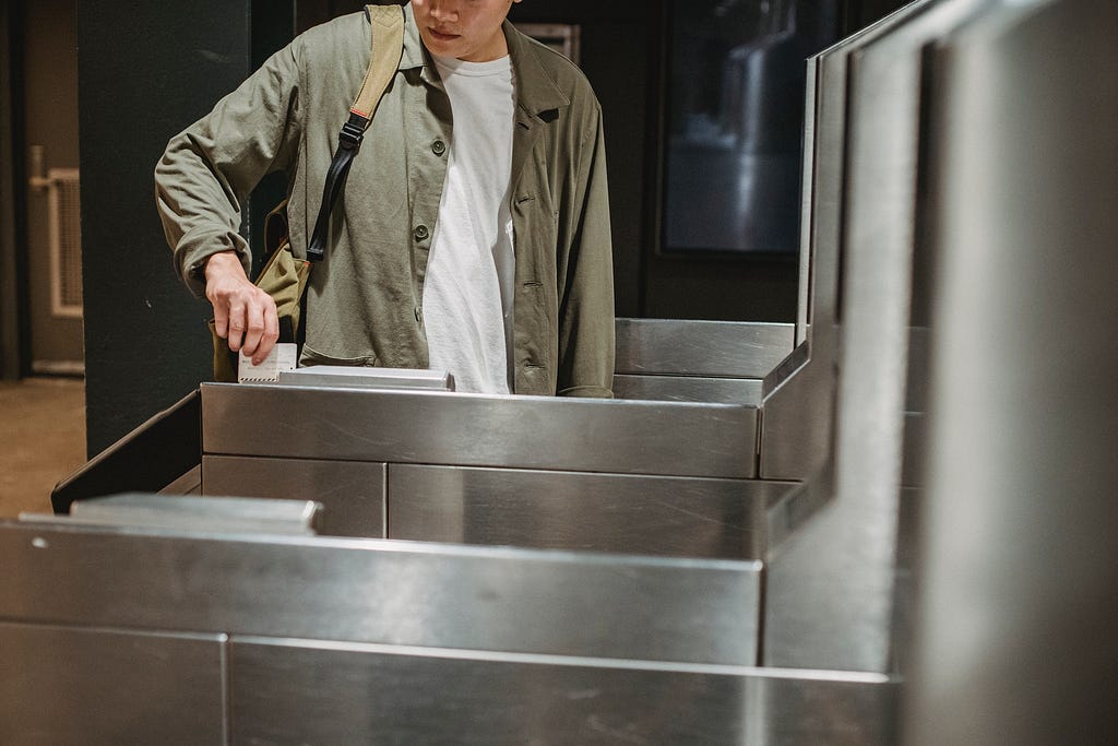 Man is sliding his metro card in the reader and waiting for the turnstile to unlock so that he can pass through.