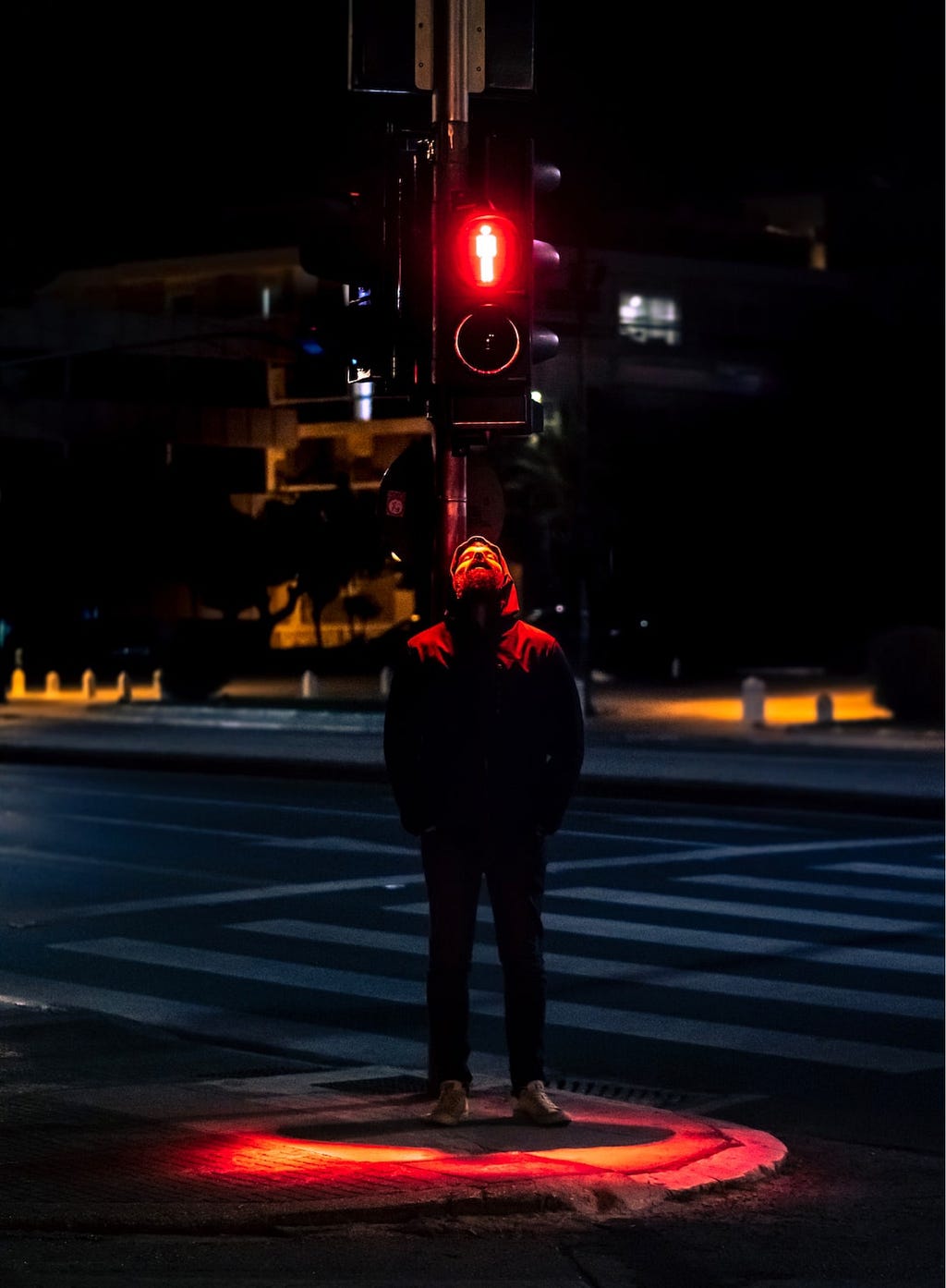 Siyah kapüşonlu bir adam, ışığının kırmızı yandığı sırada trafik direğine sırtını yaslamış ve başını göğe yükselterek derin bir nefes çekiyor.