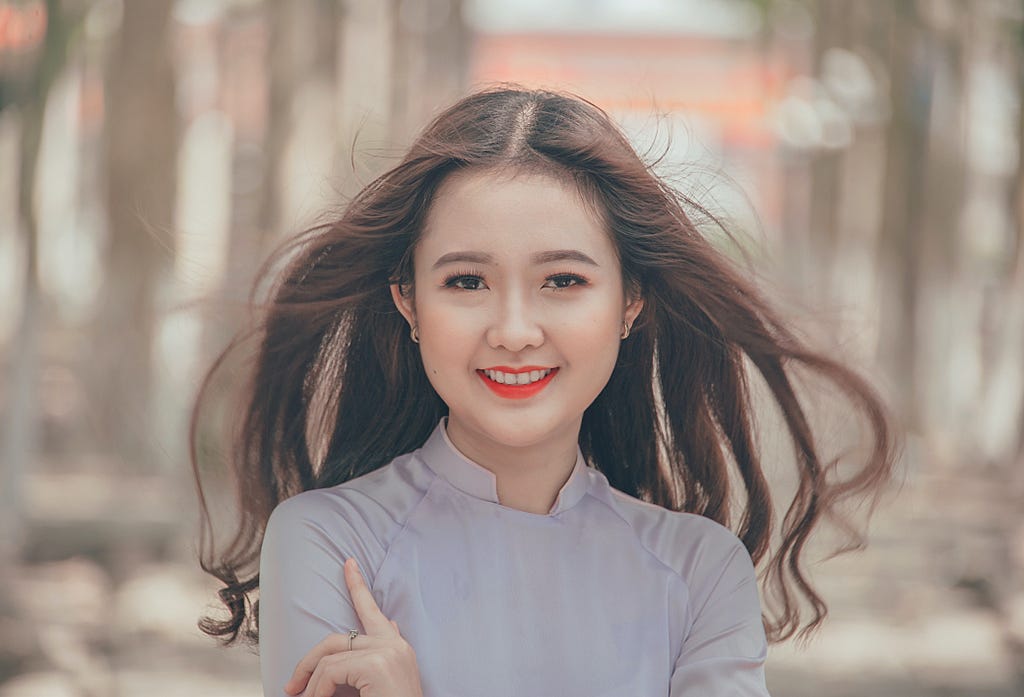 Picture of a smiling Asian girl — with long brown hair and red lipstick