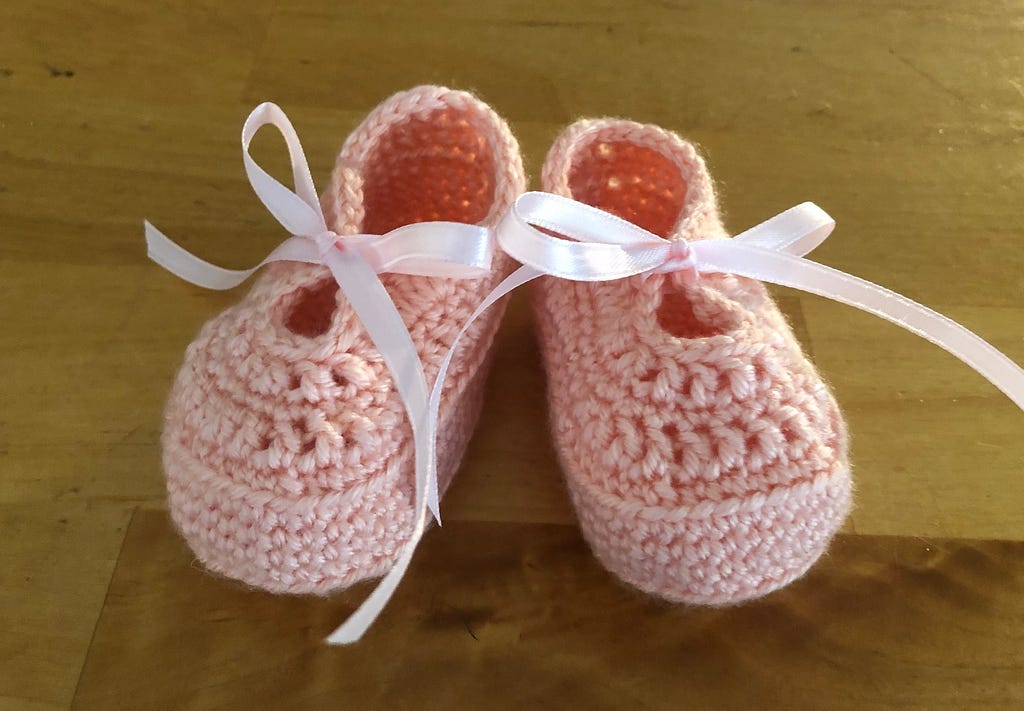 Pink, crocheted baby booties tied with pink ribbons.