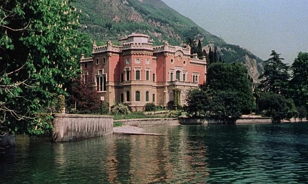 A shot of the palace from Salo from a distance, surrounded by a large body of water to the front and forestry behind. It is extravagant and beautiful.