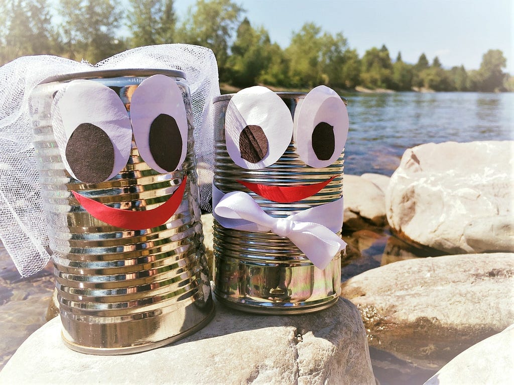 Two cans with cartoon faces are dressed up as a bride and groom.